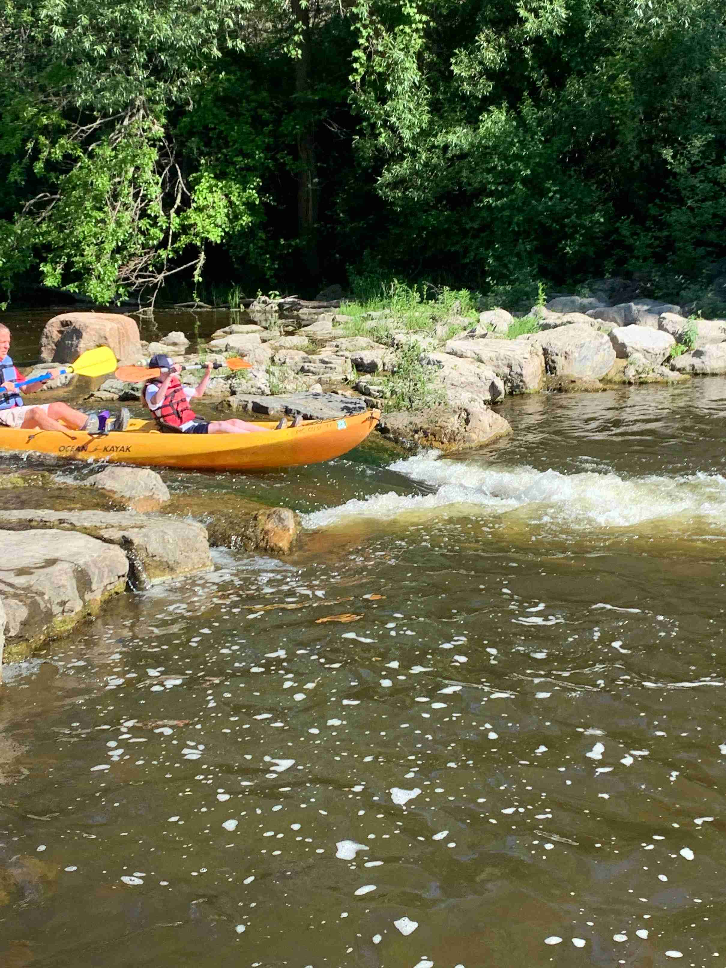 Two people on a kayak approaching some small rapids